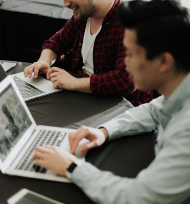 a couple of men sitting at a table with laptops