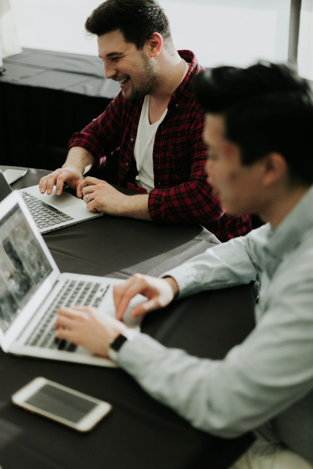 um casal de homens sentados em uma mesa com laptops