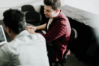 a man sitting at a desk shaking hands with another man