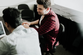 a man sitting at a desk shaking hands with another man