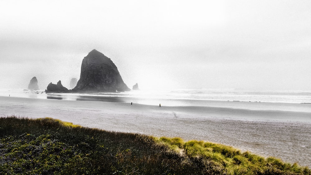 a black and white photo of a beach with a rock formation in the background