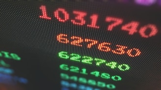 Close-up of a digital display showing brightly colored numbers with a blurred background. The numbers appear in red and green, suggesting a financial or stock market context.