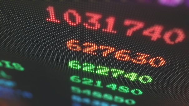 Close-up of a digital display showing brightly colored numbers with a blurred background. The numbers appear in red and green, suggesting a financial or stock market context.