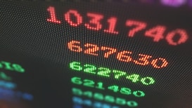 Close-up of a digital display showing brightly colored numbers with a blurred background. The numbers appear in red and green, suggesting a financial or stock market context.