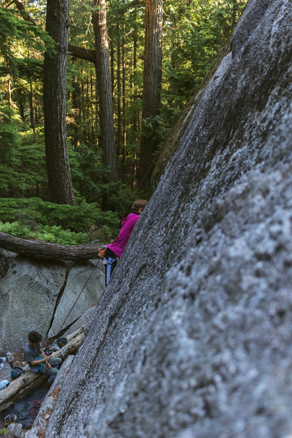 two people climbing up a rock in the woods