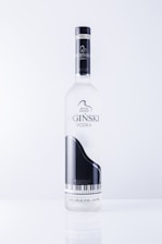 A vodka bottle featuring a sleek design with a black and white grand piano image. The label includes text in an elegant font and highlights the name 'OGINSKI VODKA'. The bottle is clear and sits against a plain, light background.