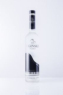 A vodka bottle featuring a sleek design with a black and white grand piano image. The label includes text in an elegant font and highlights the name 'OGINSKI VODKA'. The bottle is clear and sits against a plain, light background.