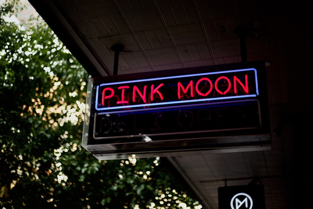 a pink moon sign hanging from the side of a building