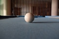 A solitary billiard ball rests on a pool table with a focus on the texture of the felt. The background features vertical wooden bars, creating a sense of depth.