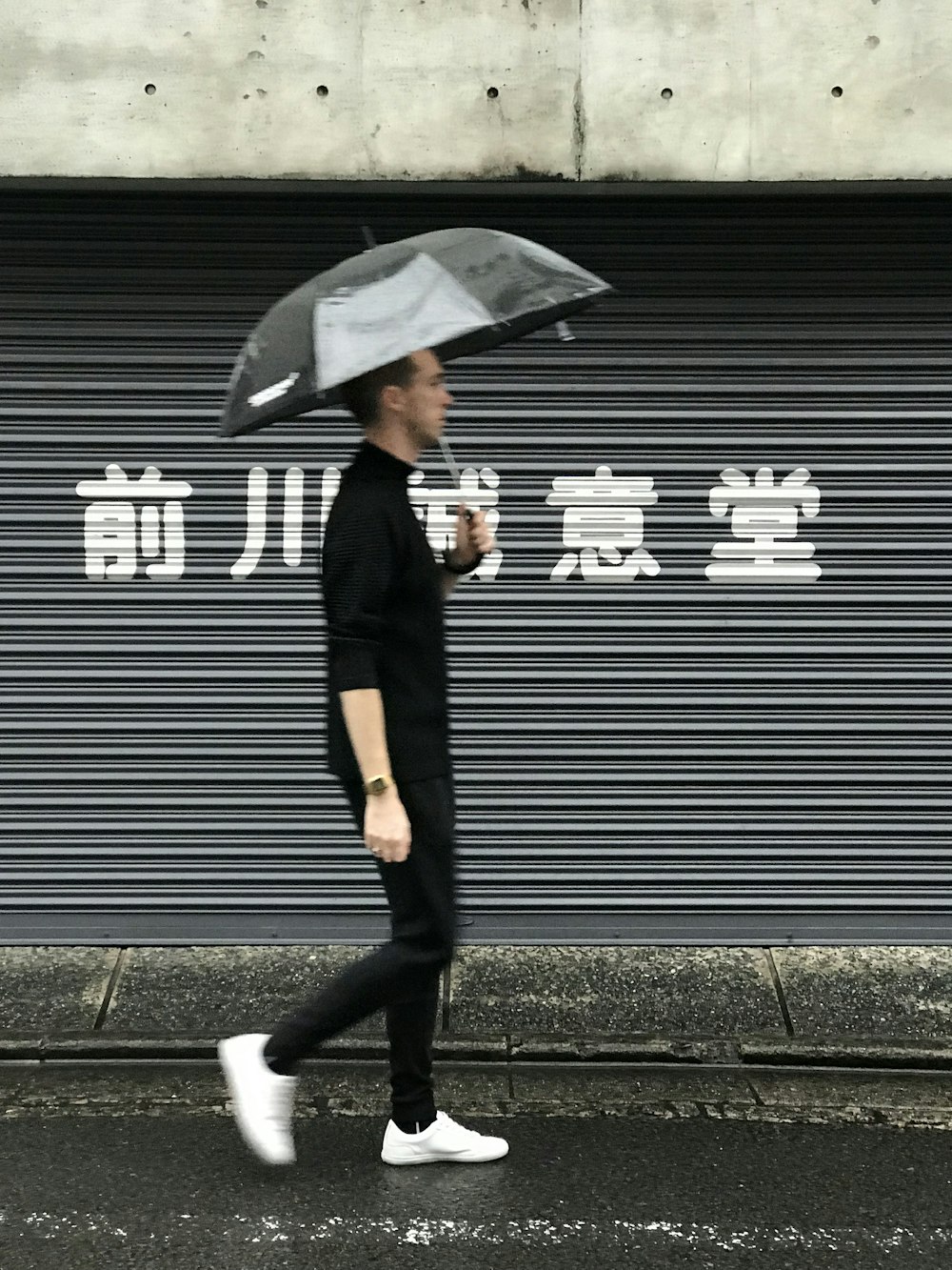 woman in black coat and black pants holding umbrella walking on sidewalk during daytime