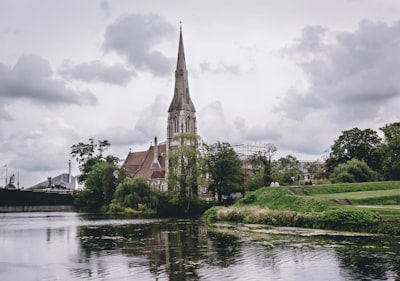 brown and gray concrete building near body of water under cloudy sky during daytime neoclassical teams background