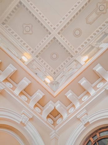 An ornate ceiling with intricate architectural details including moldings, decorative patterns, and recessed lighting. The design features symmetrical geometric shapes and relief decorations, conveying a sense of elegance and classical architecture.