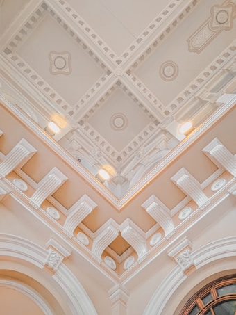 An ornate ceiling with intricate architectural details including moldings, decorative patterns, and recessed lighting. The design features symmetrical geometric shapes and relief decorations, conveying a sense of elegance and classical architecture.