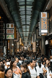 A bustling shopping complex corridor with colorful storefronts and shoppers browsing.