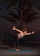 A woman performs a yoga pose on a blue mat, balancing on one leg while holding her other foot with one hand. Palm trees and a dark twilight sky form the backdrop.