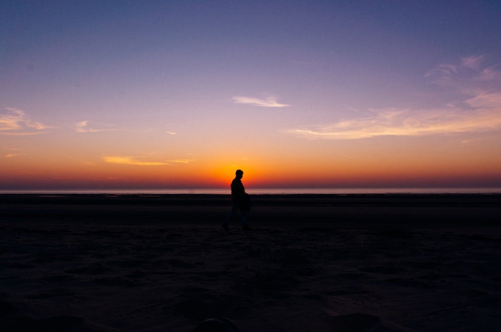 a person walking on a beach at sunset