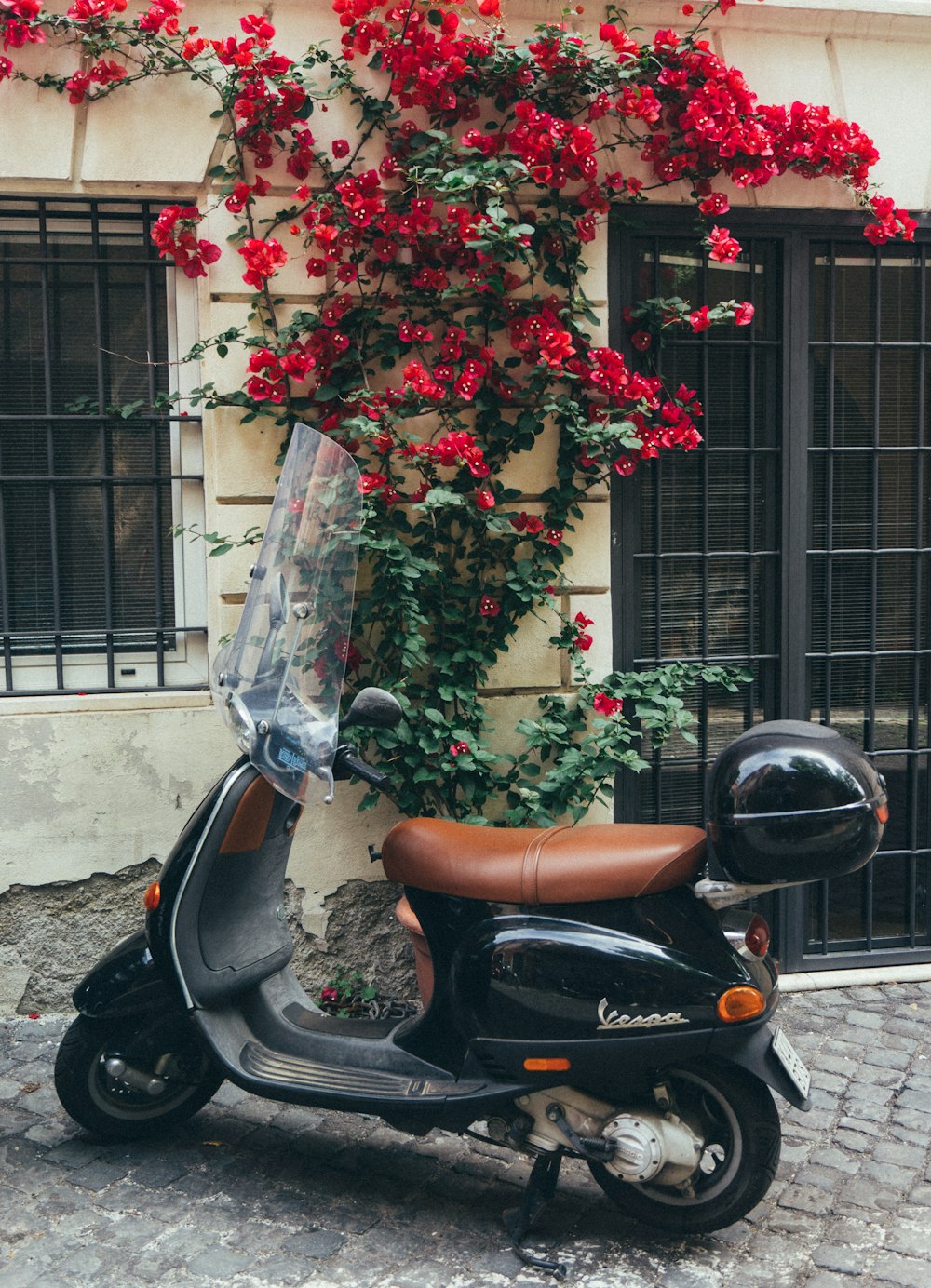 uma scooter estacionada em frente a um prédio com flores vermelhas