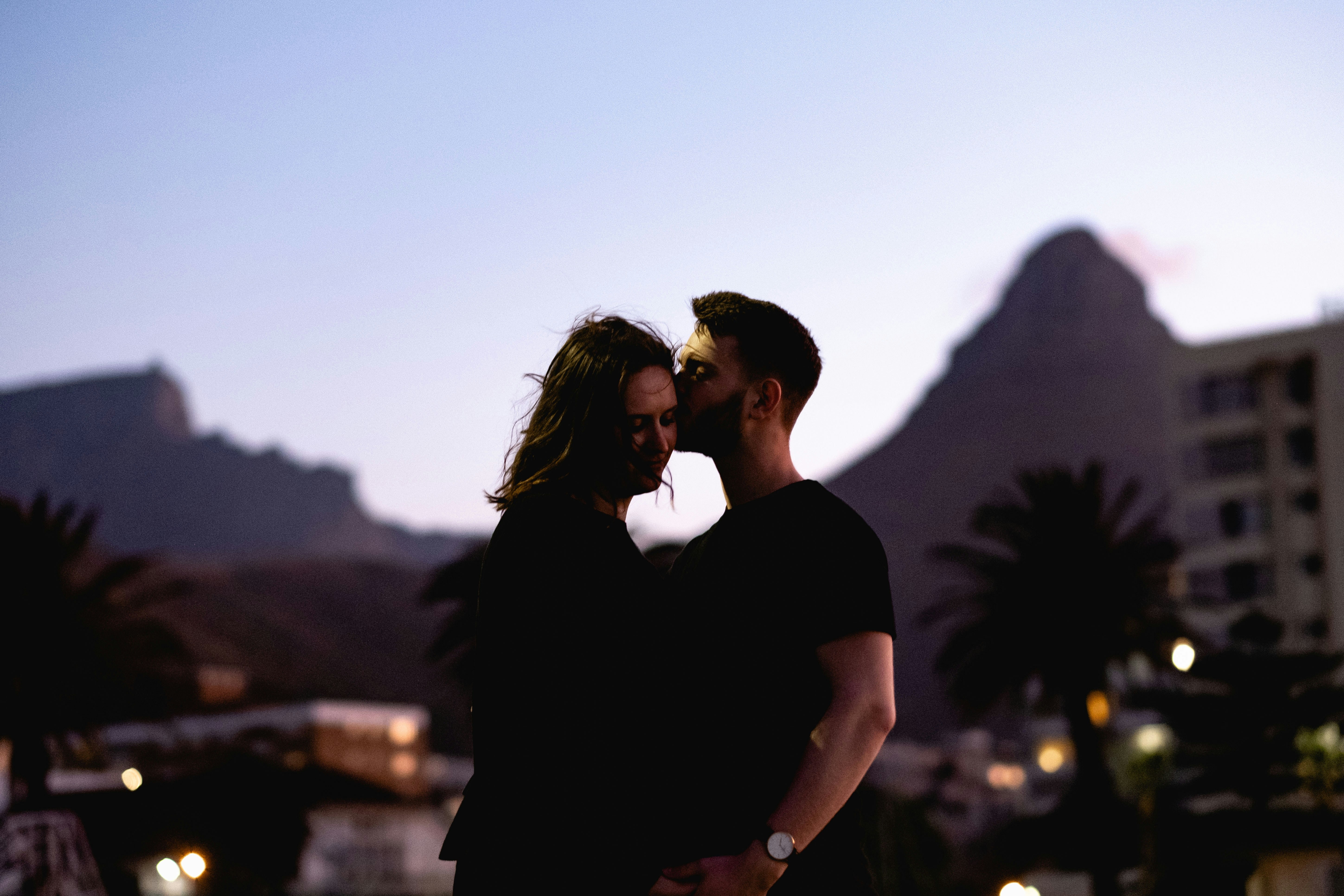 man in black t-shirt kissing woman in black dress during daytime