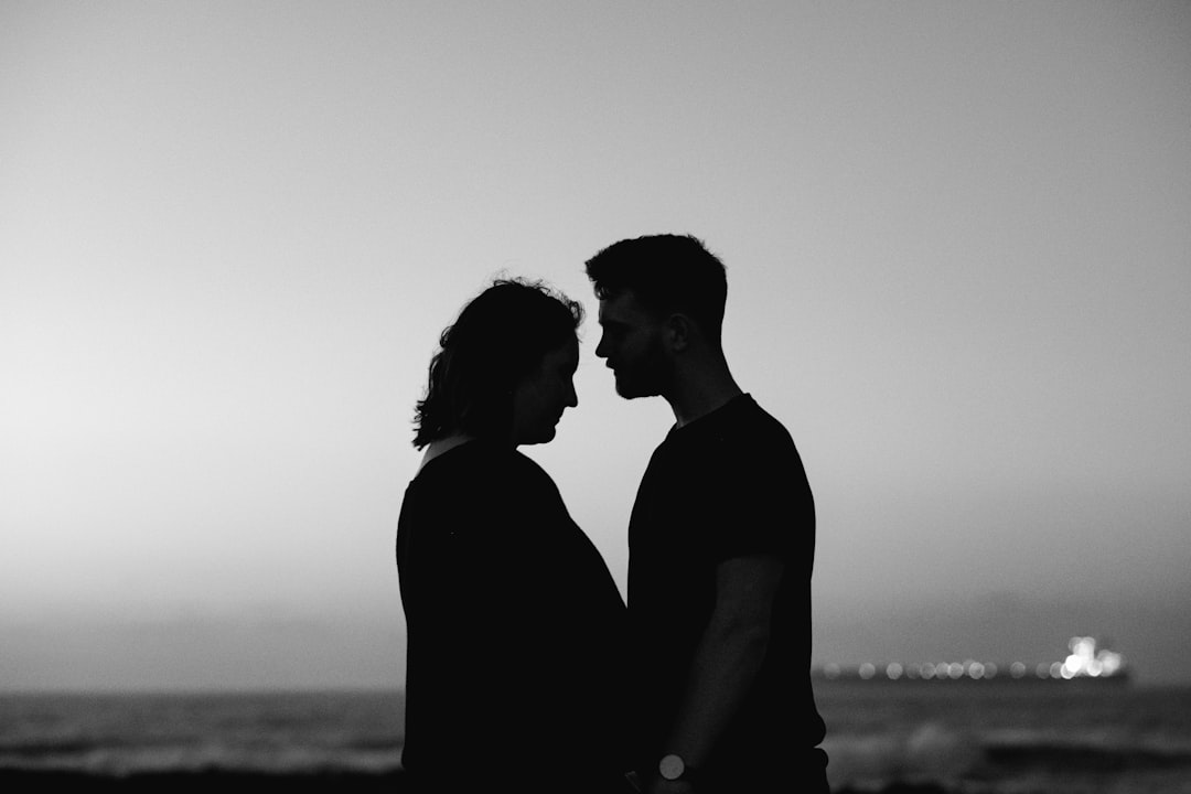 silhouette of man and woman standing near body of water during daytime