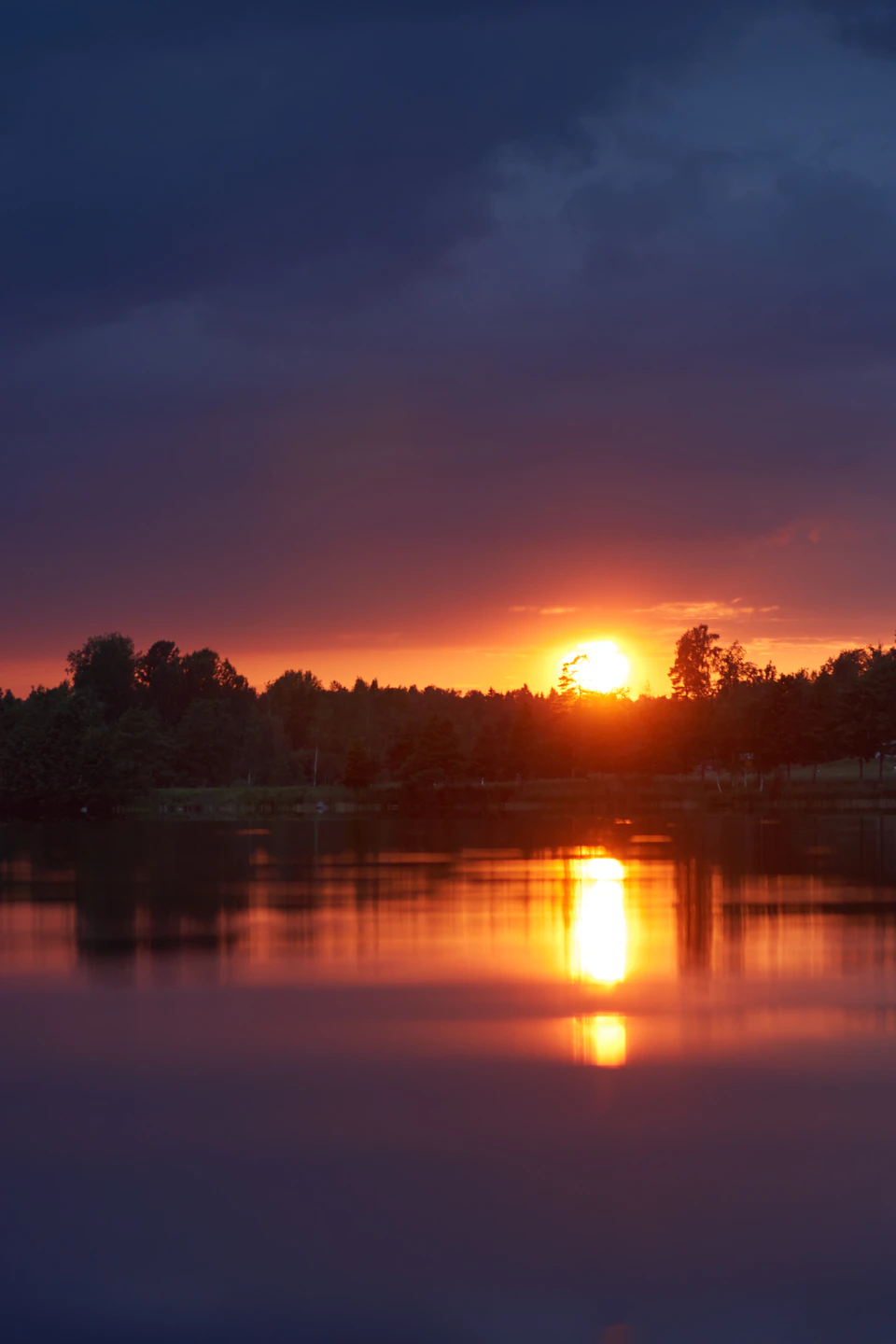 Serene sunset over water with trees and warm glow behind a cluster of trees