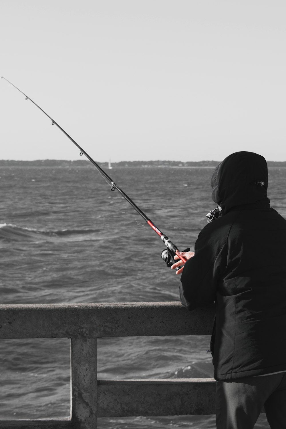 Persona in felpa con cappuccio nera che pesca in mare durante il giorno