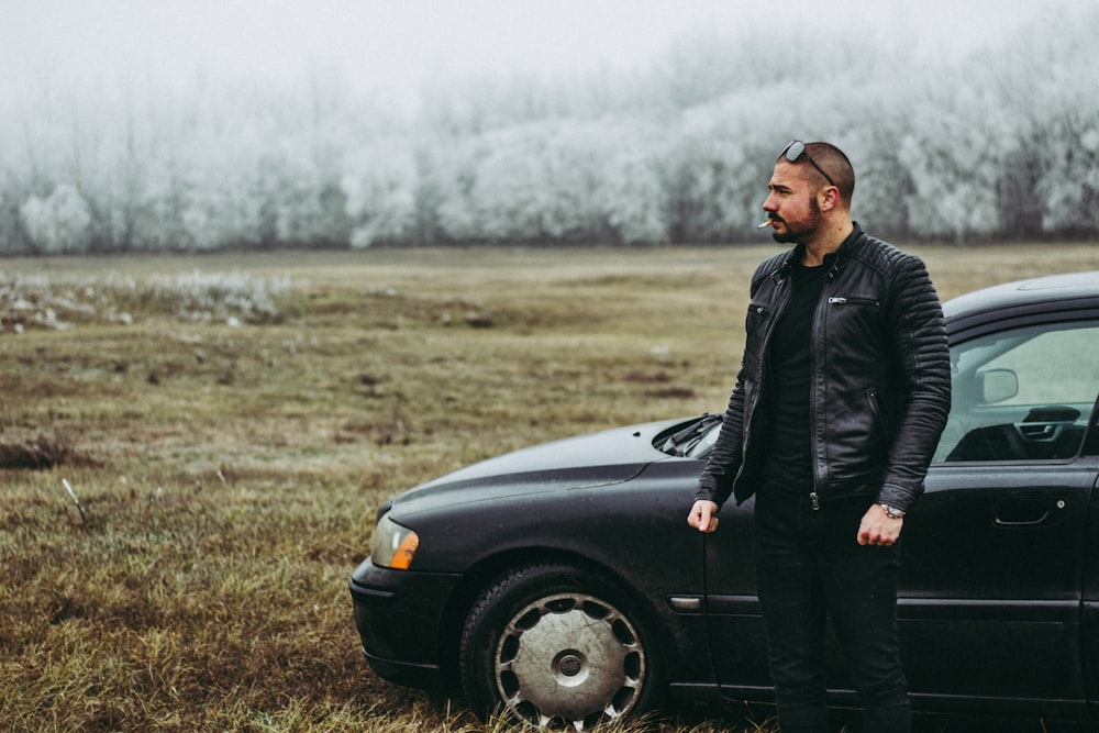 man in black jacket standing beside black car during daytime