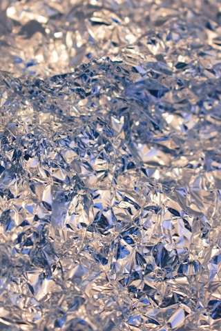 Crumpled silver foil creating a textured, reflective surface with intricate folds and creases.