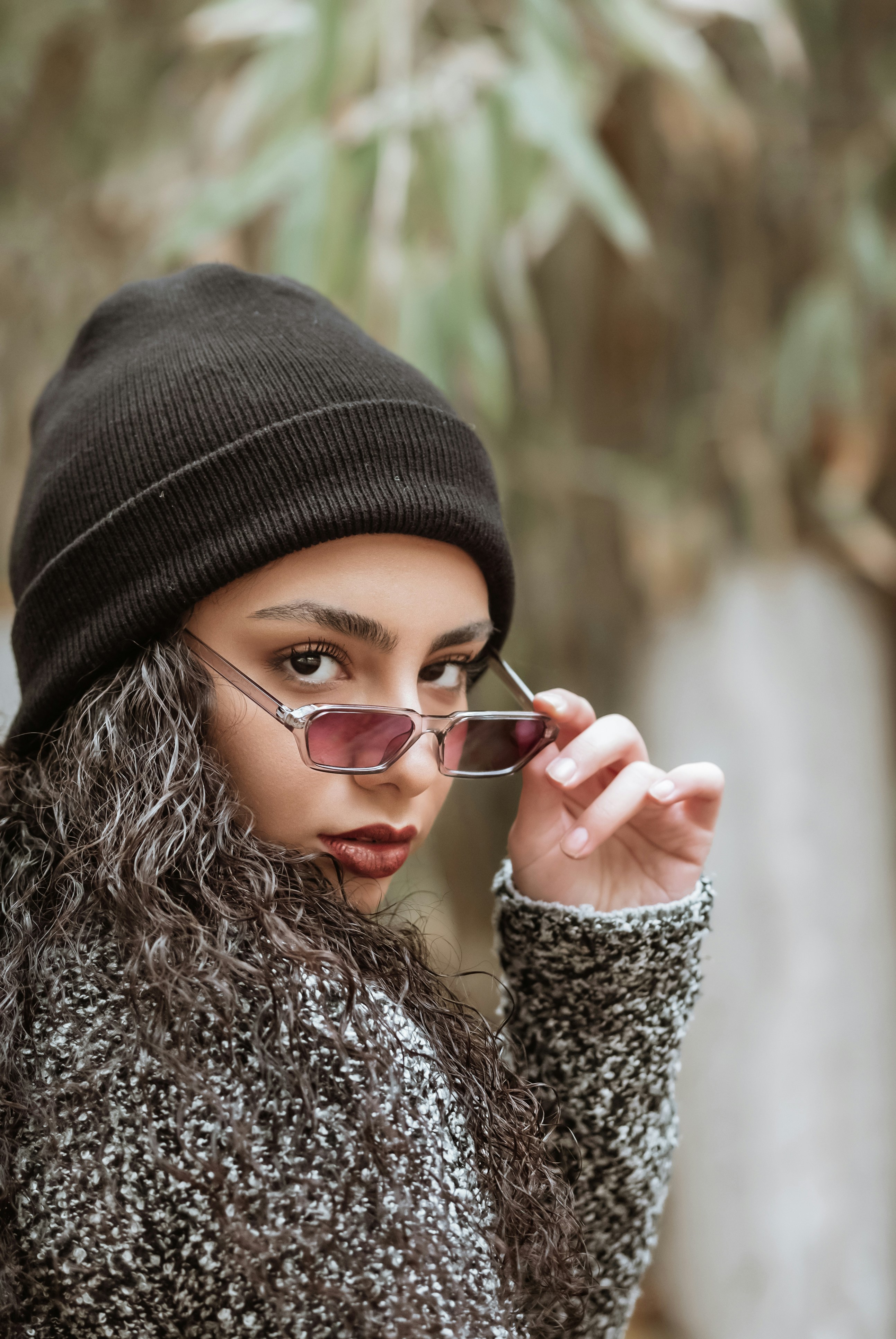 a woman wearing a beanie and glasses talking on a cell phone