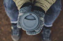 A person wearing sleek leather gloves while holding a steaming cup of coffee outdoors in autumn.