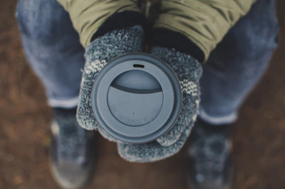 A person wearing sleek leather gloves while holding a steaming cup of coffee outdoors in autumn.
