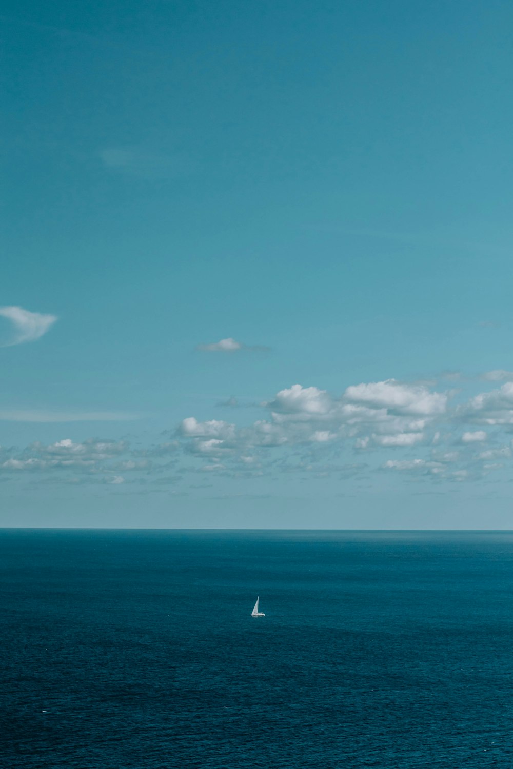 white sailboat on sea under blue sky and white clouds during daytime