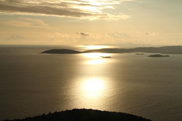 Sunset casting golden light over a calm sea with distant islands on the horizon.