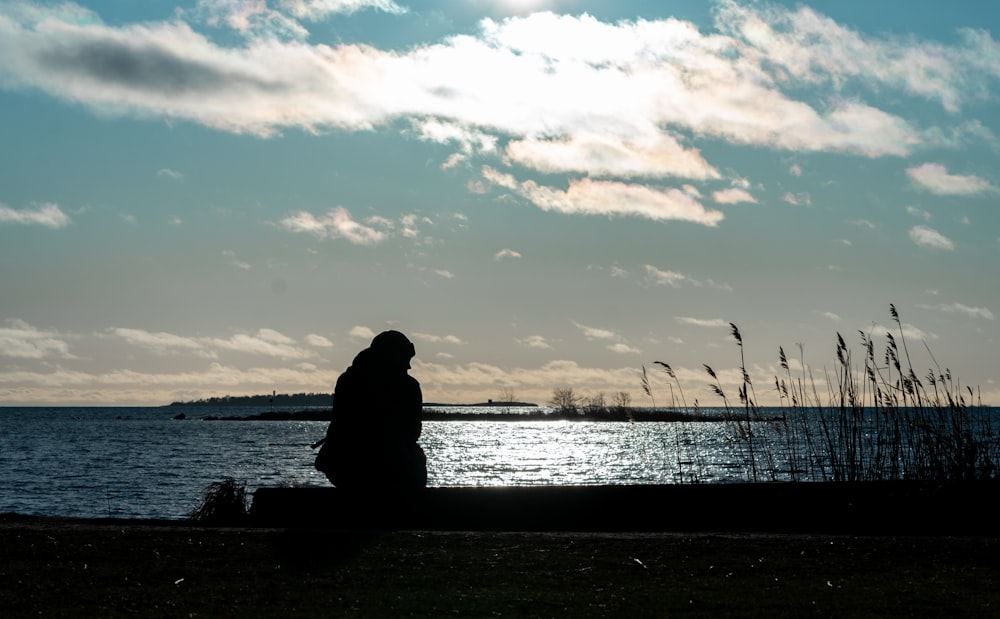 silhueta da pessoa sentada no banco perto do corpo de água durante o pôr do sol