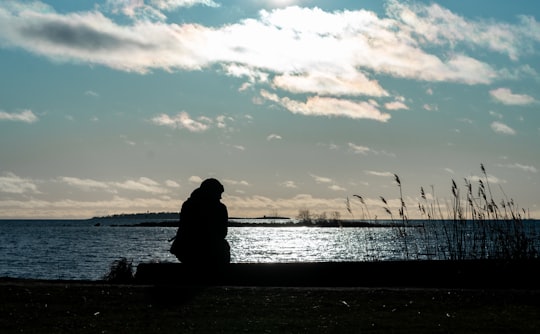silhouette of person sitting on bench near body of water during sunset in Lauttasaari Finland