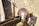A medieval helmet and sword rest on a wooden structure against a stone wall. The helmet is metallic with rivets and detailed craftsmanship, while the sword has a simple, sturdy handle and blade.