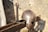 A medieval helmet and sword rest on a wooden structure against a stone wall. The helmet is metallic with rivets and detailed craftsmanship, while the sword has a simple, sturdy handle and blade.