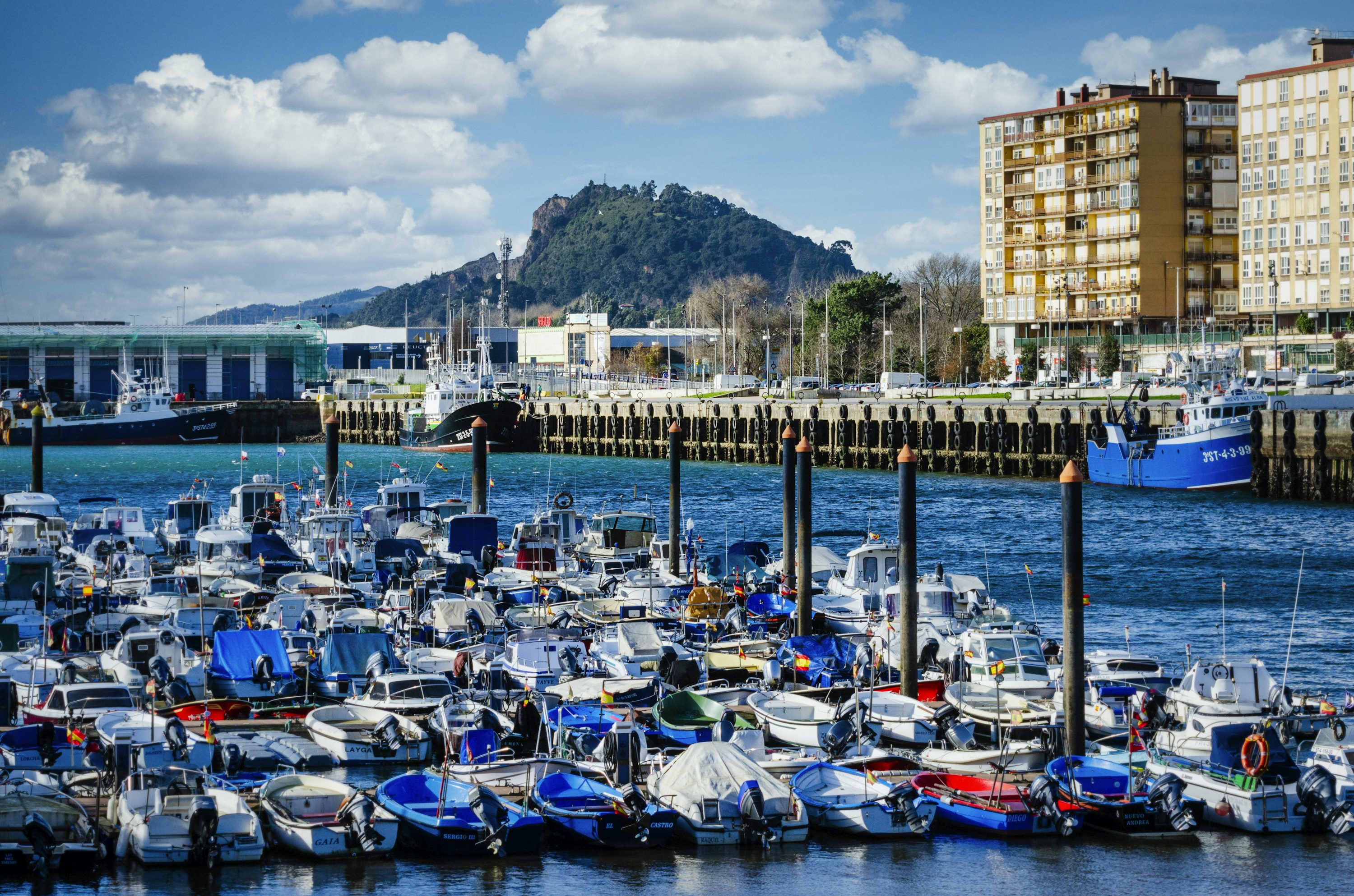barcos azules y blancos en el muelle cerca de los edificios de la ciudad bajo un cielo nublado soleado azul y blanco