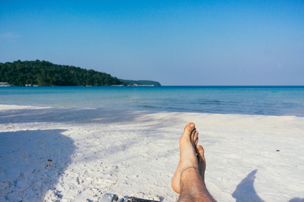 a person laying on a beach with their feet in the sand