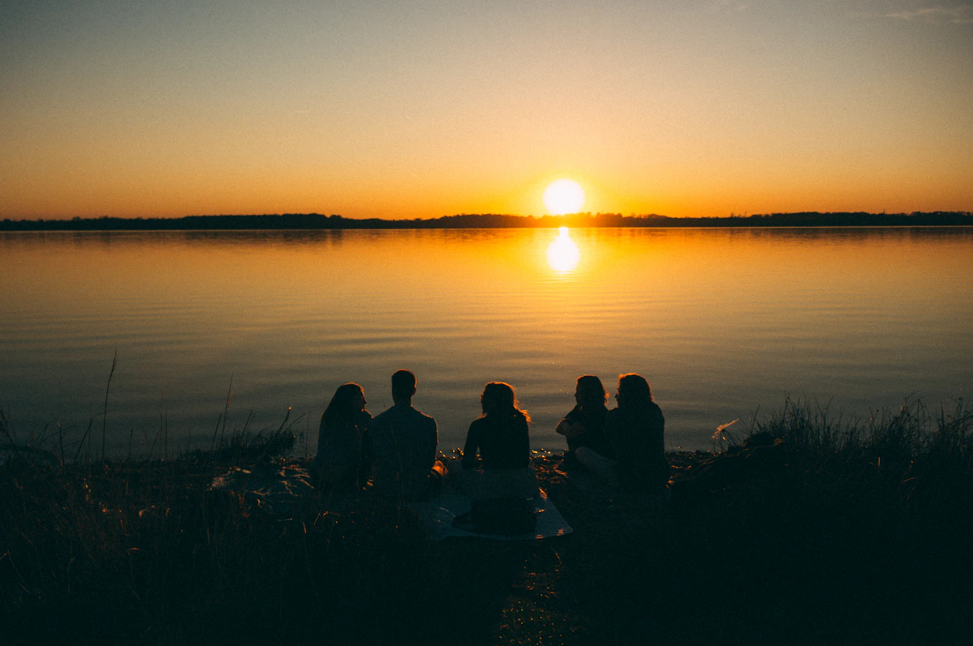 Un groupe d'amis assis au bord d'un lac au coucher du soleil.