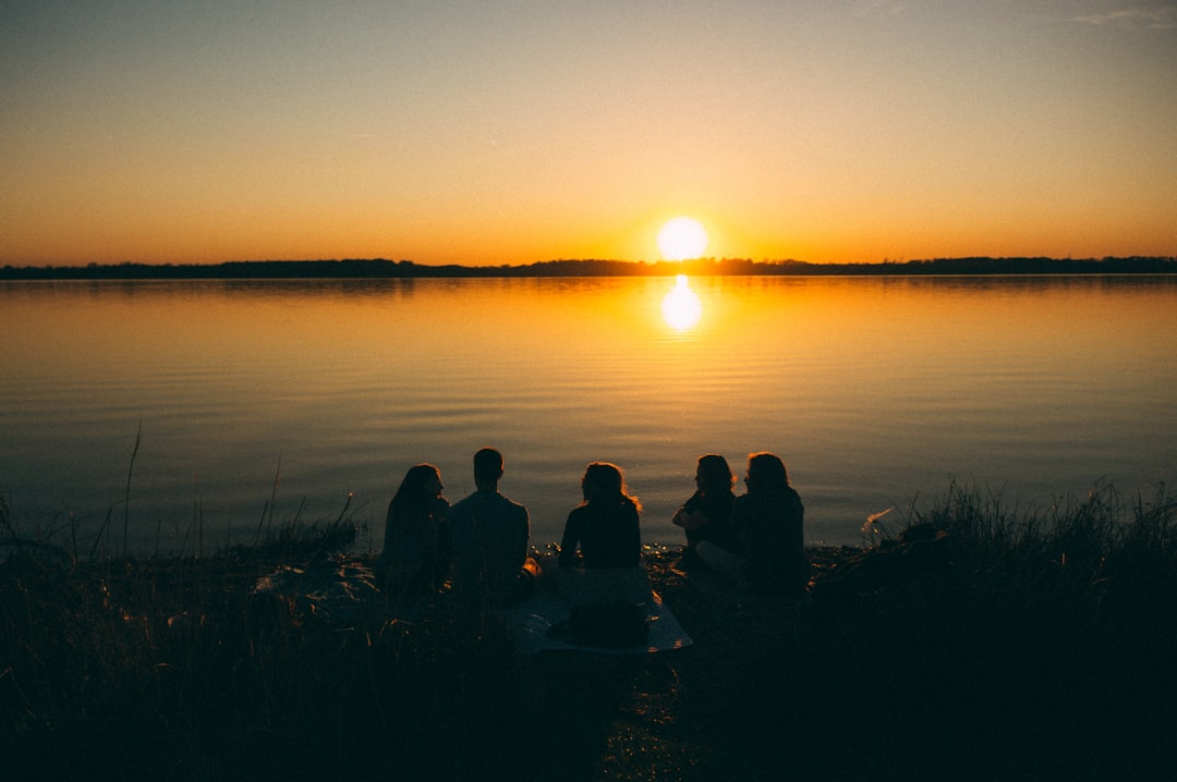 a group of people sitting on the shore of a lake at sunset, those nights