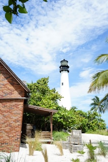 brown and white concrete lighthouse near green palm tree under blue sky during daytime