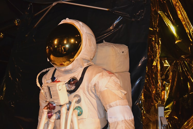 A spacesuit with a golden mirrored visor standing in front of gold foil