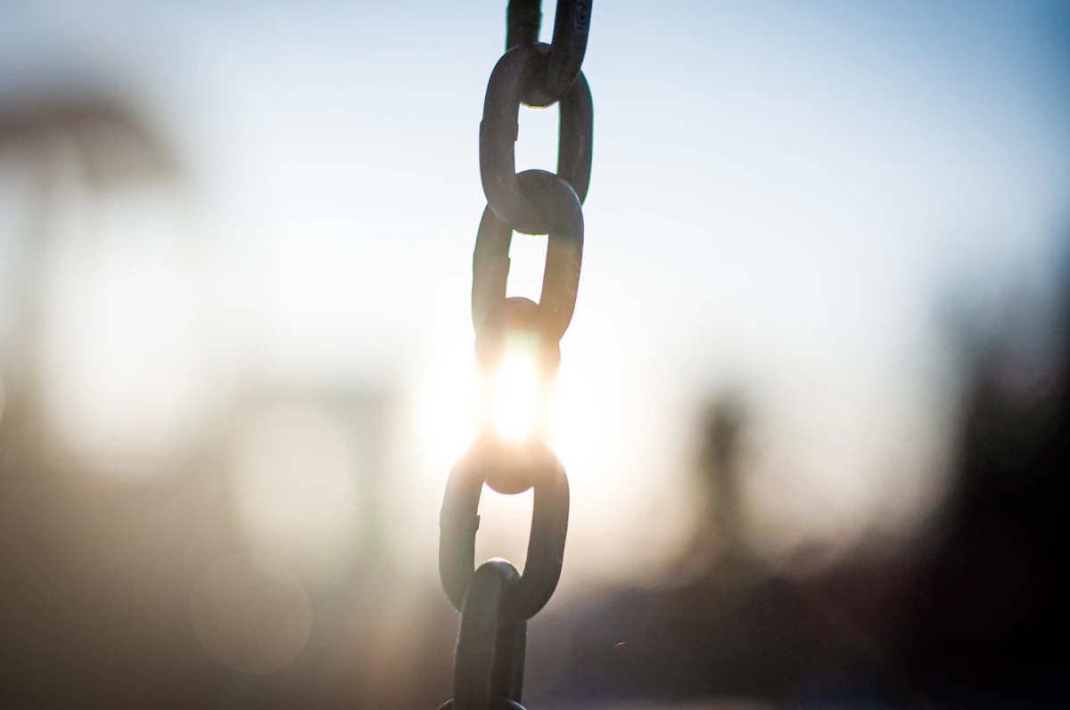 Backlit metal chain links with sunlight passing through a single gap between two of the links, rather than along the whole length of the chain
