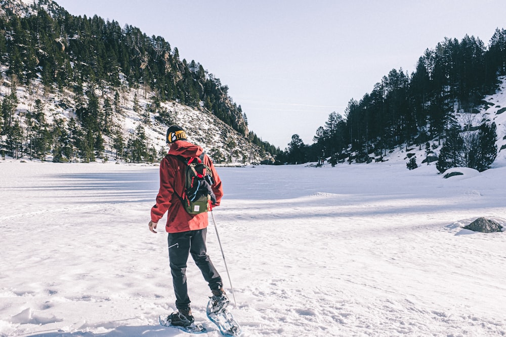 man in red jacket and blue denim jeans standing on snow covered ground during daytime