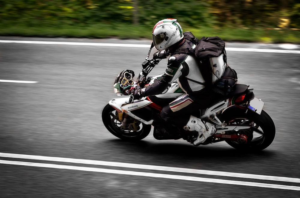 昼間の道路でオートバイに乗る黒と白のオートバイのスーツを着た男
