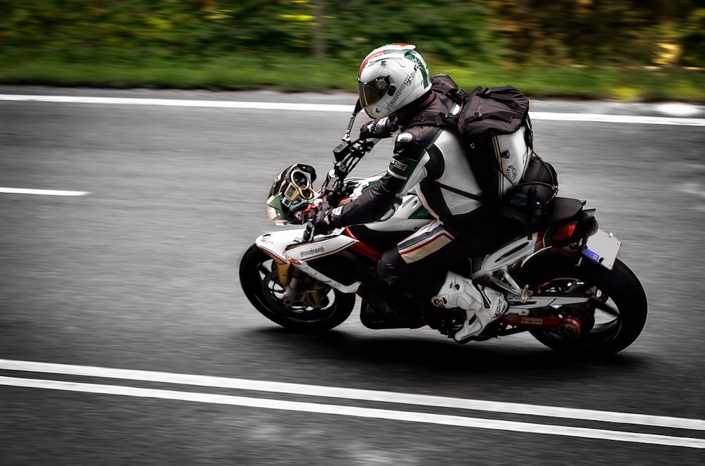 uomo in abito da motociclista bianco e nero che guida la moto sulla strada durante il giorno