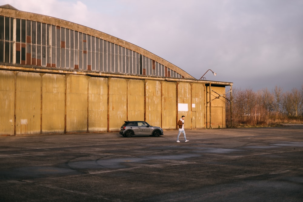 man in white shirt and white pants walking on street near black car during daytime