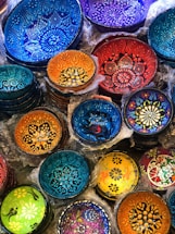 A collection of intricately designed decorative bowls with vibrant colors and patterns. The bowls feature floral and geometric designs, with each one displaying unique artistry and color combinations. They are stacked and nestled with packaging material around them.