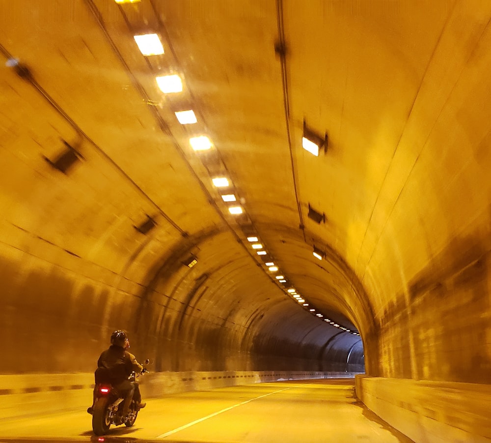 man in black jacket and black pants walking on tunnel