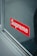 A reflective surface displays a red sticker with the brand name 'Supreme' in bold white letters. The sticker appears to be affixed onto a glass pane, with metallic or wooden trim visible along the edges.